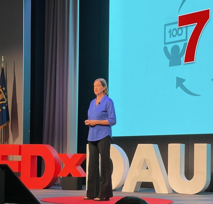 Image of Emily Harman, author of the blog post "7 Lessons Learned from My TEDx Talk Adventure: Embracing Growth, Inspiring Change, and Making a Lasting Impact." Emily is a speaker, coach, and author who helps people to embrace growth and make a difference in the world. She is standing in front of a microphone, giving a speech.